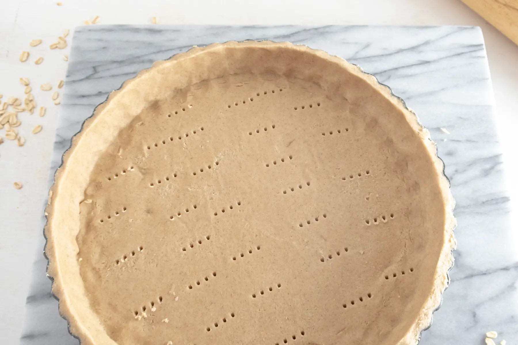 View the bottom of a raw tart shell that is pricked by a fork all over.