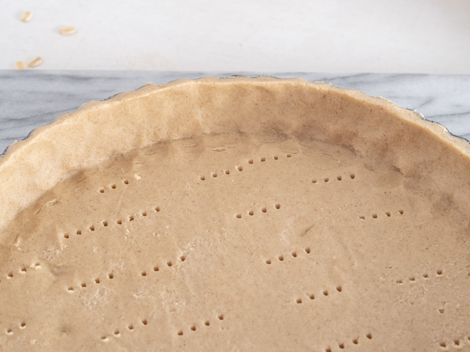 Close up of the bottom of a raw tart shell that is pricked by a fork all over.