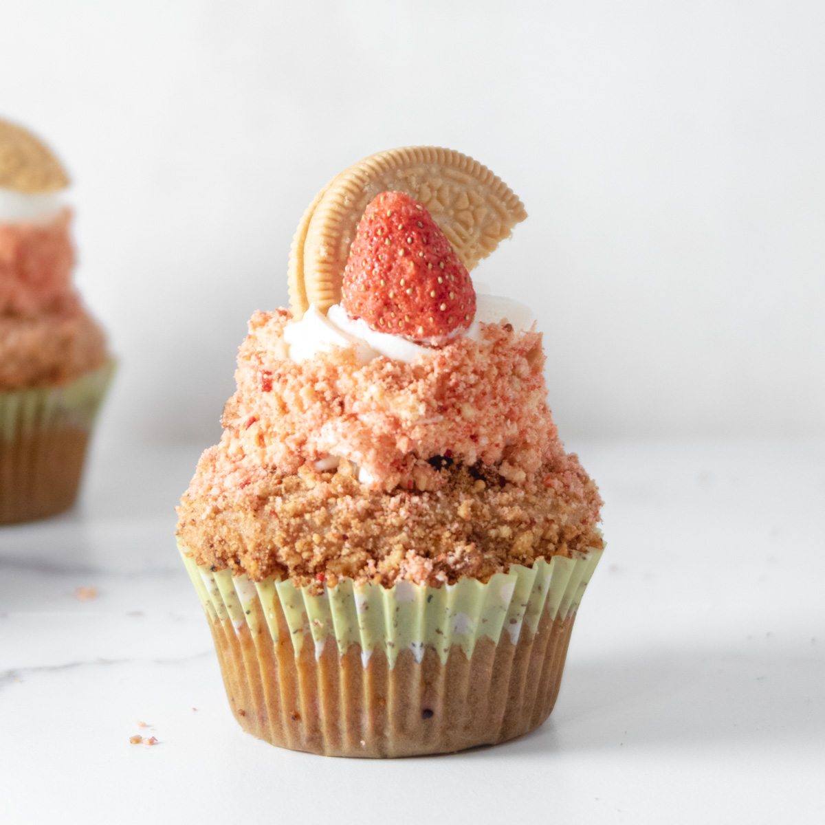 Strawberry crunch cupcake topped with a half golden oreo and freeze dried strabwerry in front of a white backgorund.