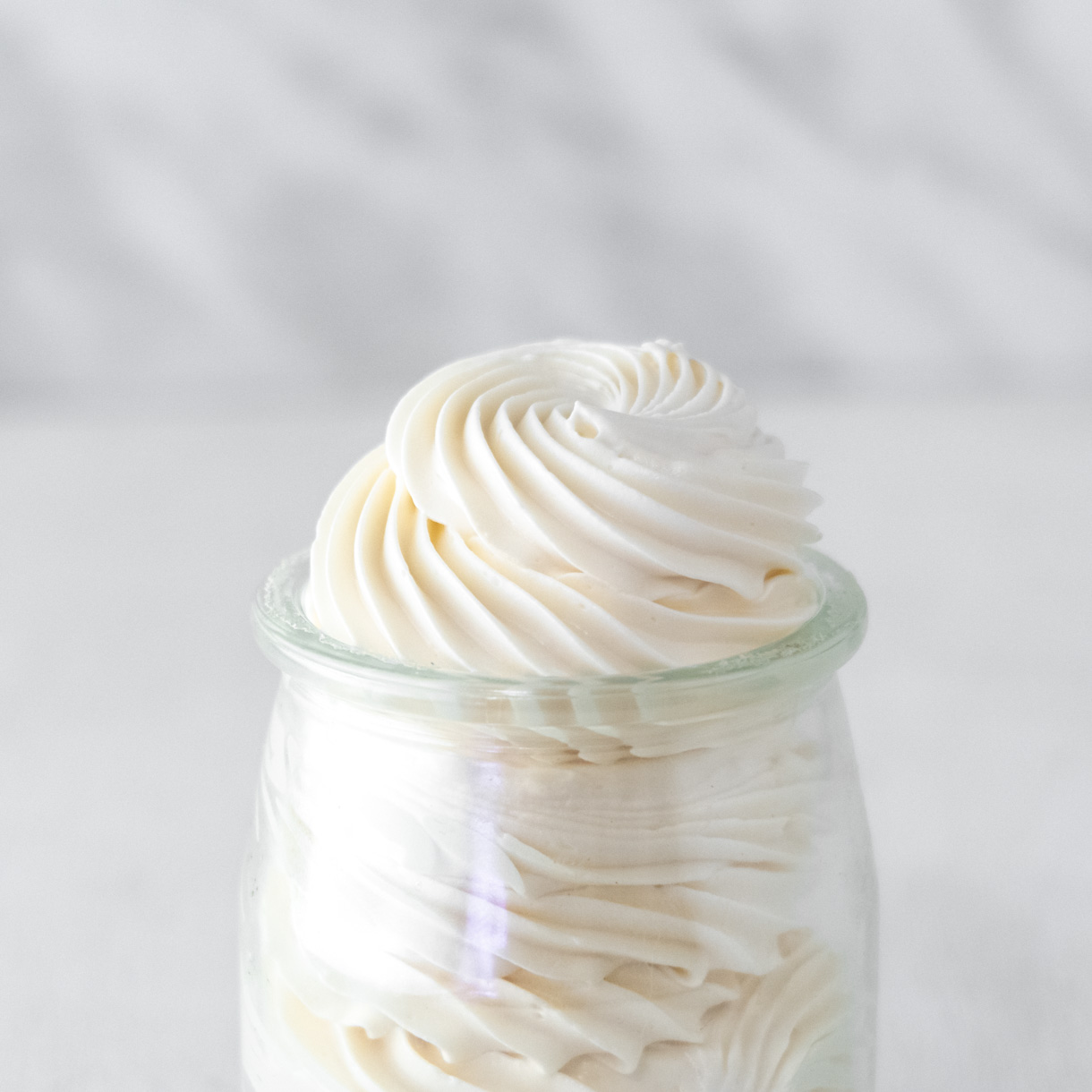 Close up of vegan Italian meringue buttercream piped in a small glass jar.