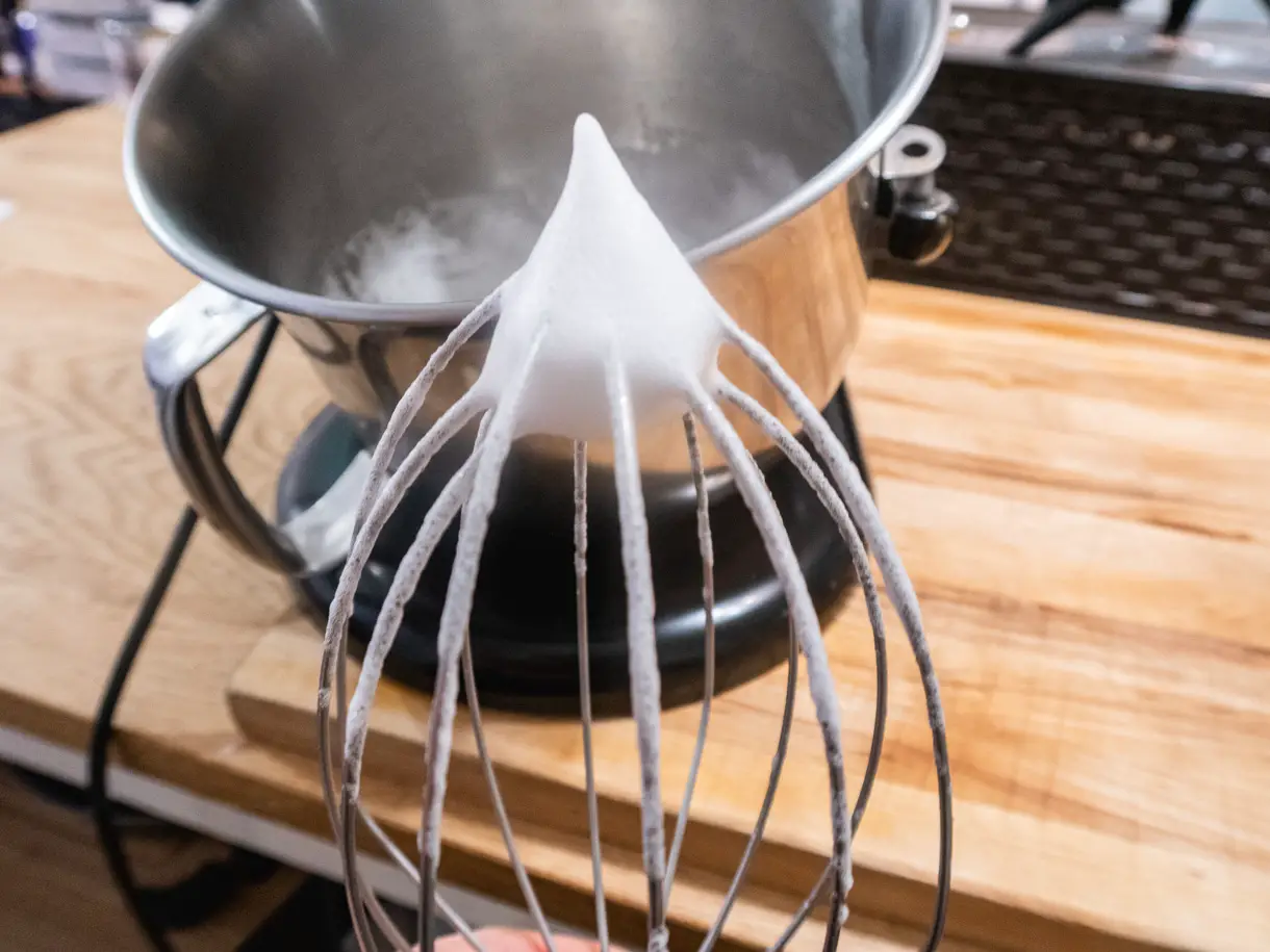 Whipped aquafaba foam on a whisk before adding the sugar syrup