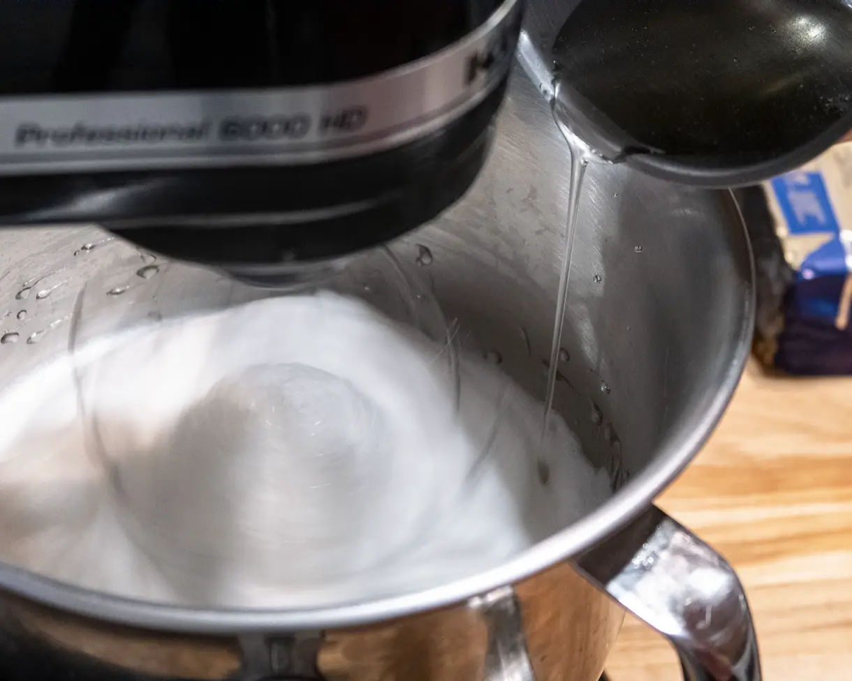 Sugar syrup being slowly added in a stream into the bowl of a stand mixer with merinuge