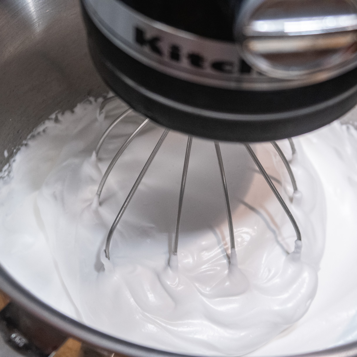 Italian meringue "climbing" up the whisk of a stand mixer.