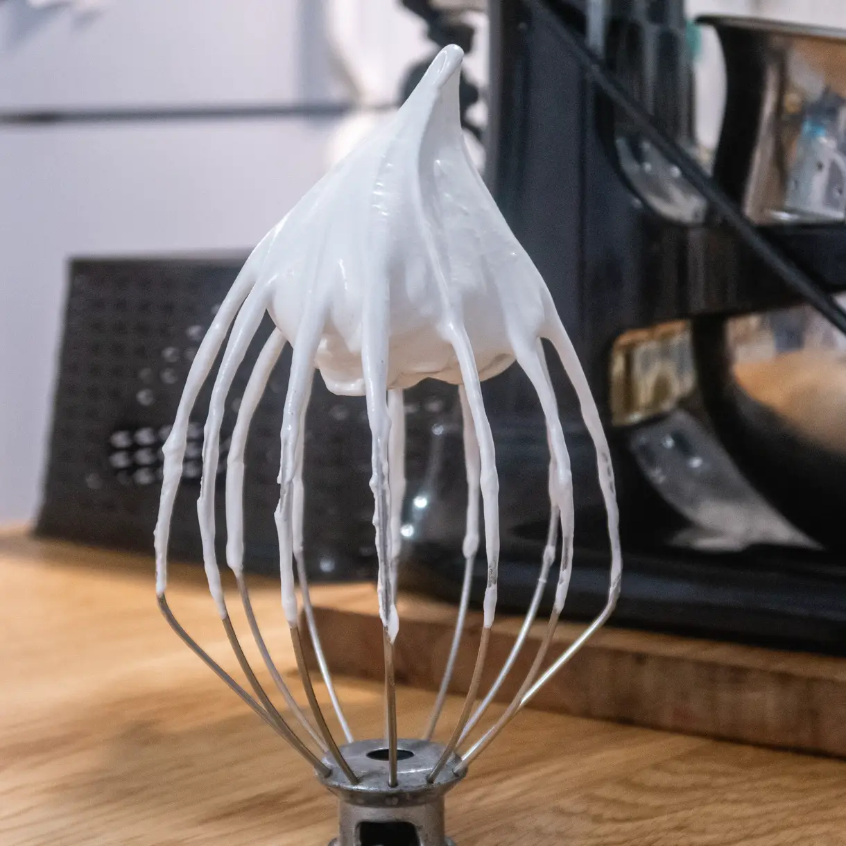 Thick and glossy vegan Italian meringue standing straight up on the whisk of a stand mixer.