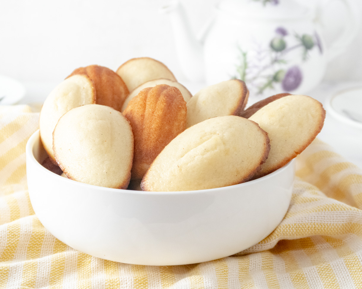 Vegan lemon madeleines layered in a white bowl on a yellow tablecloth.
