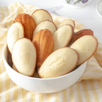 Vegan lemon madeleines layered in a white bowl on a yellow tablecloth.