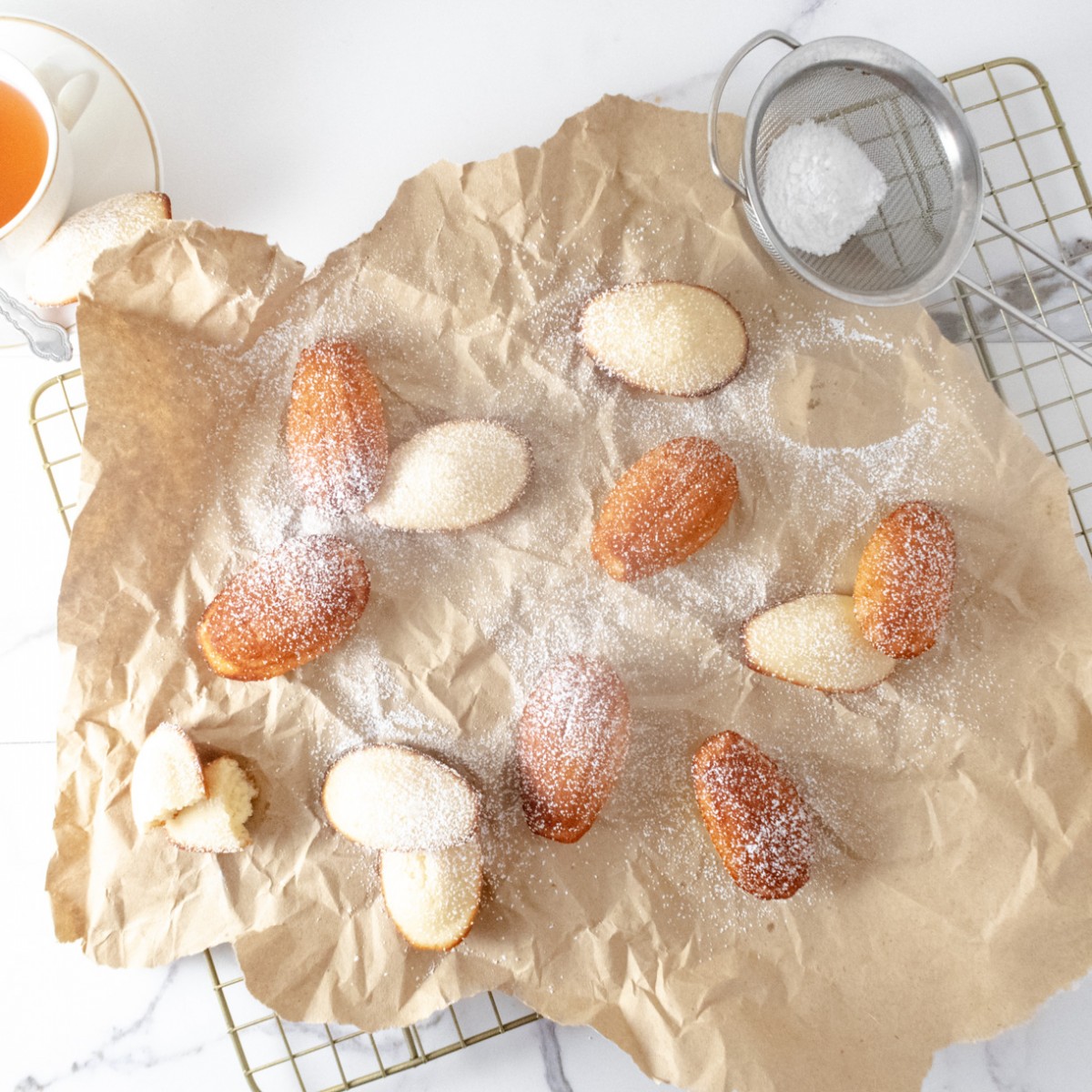 Madeleines lightly dusted with powdered sugar on a piece of kraft paper on a wire rack.