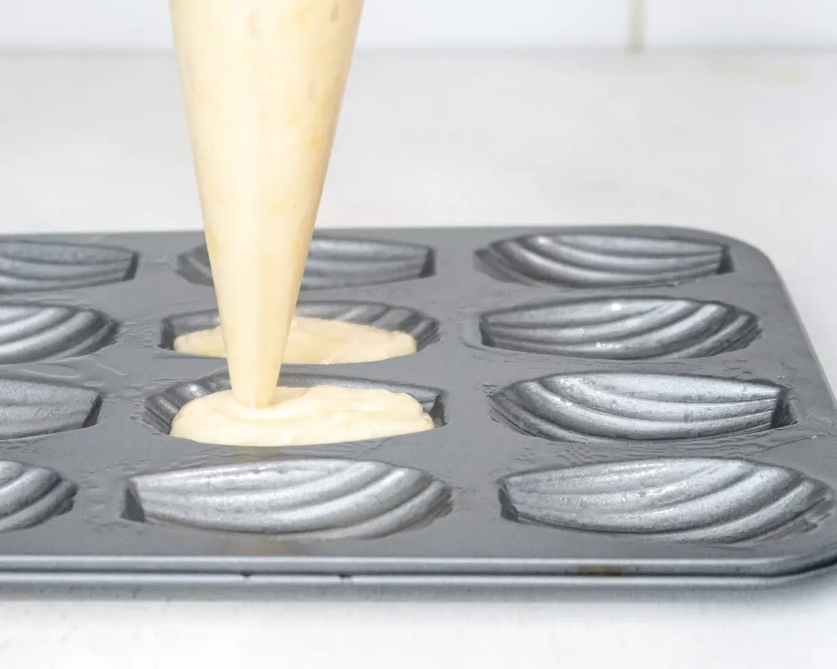 Vegan madeleine batter in a piping bag being pipped in a madeleine baking tray