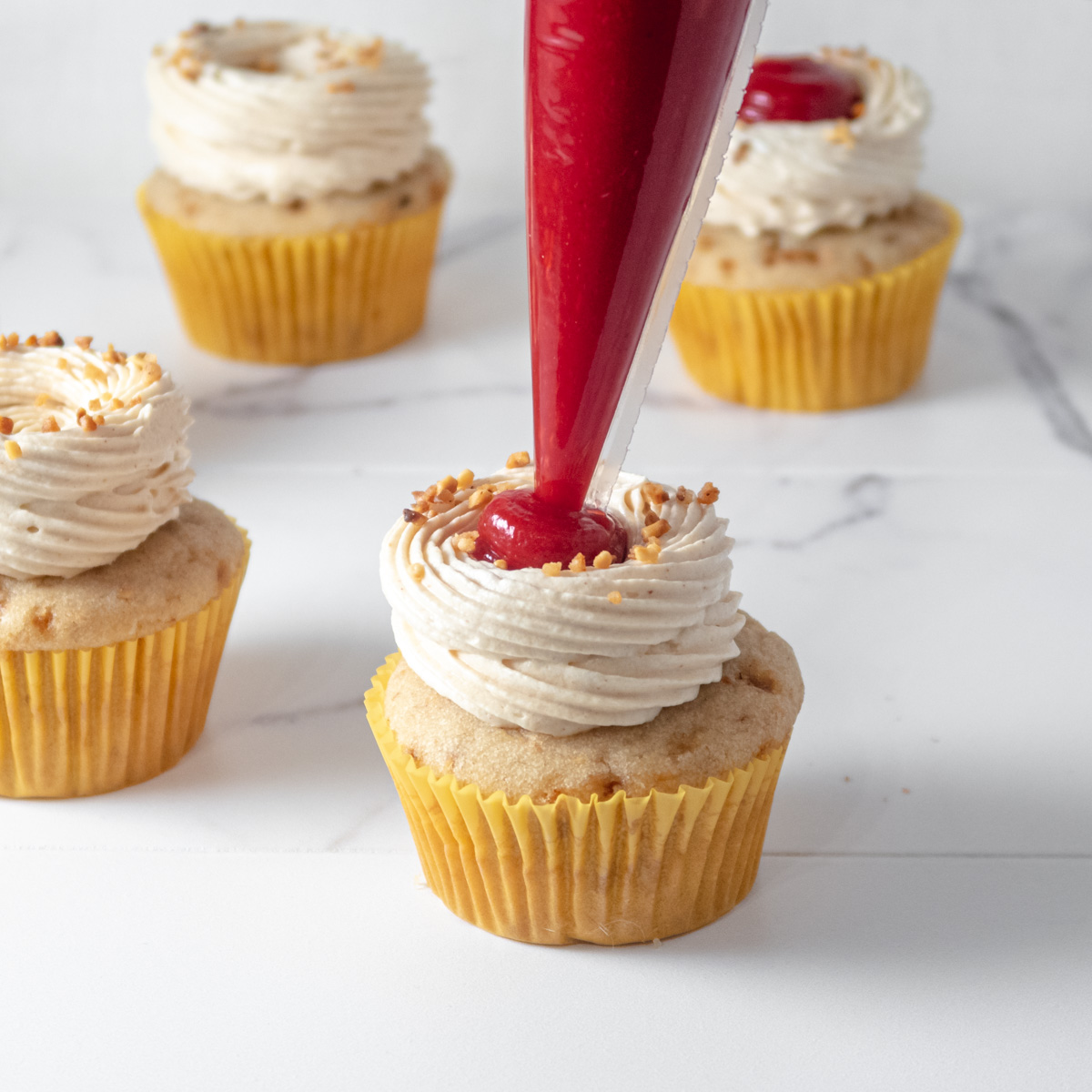 Seedless raspberry curd being piped on top of vegan peanut butter cupcakes.