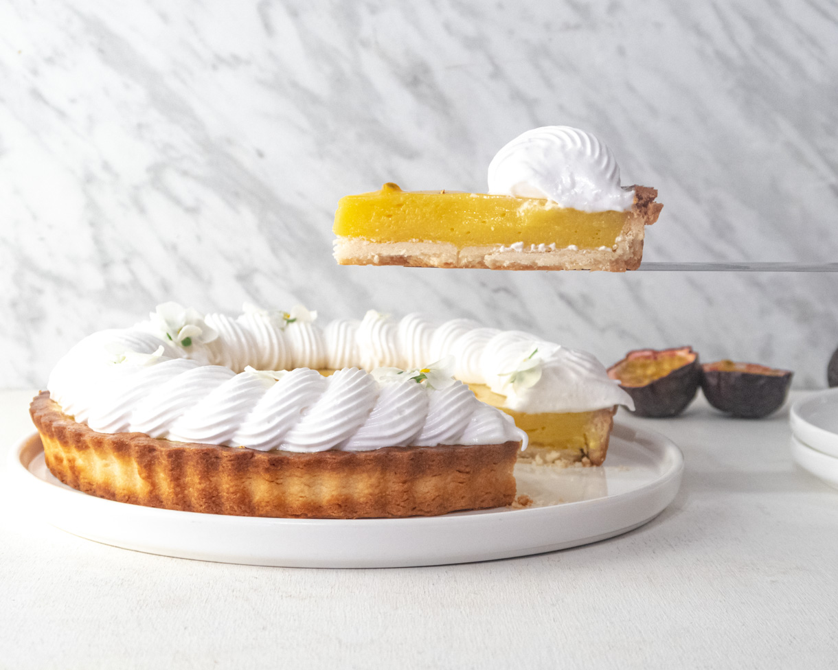 A slice of passionfruit tart being held up in the air on a knife on top of the rest of the tart. 