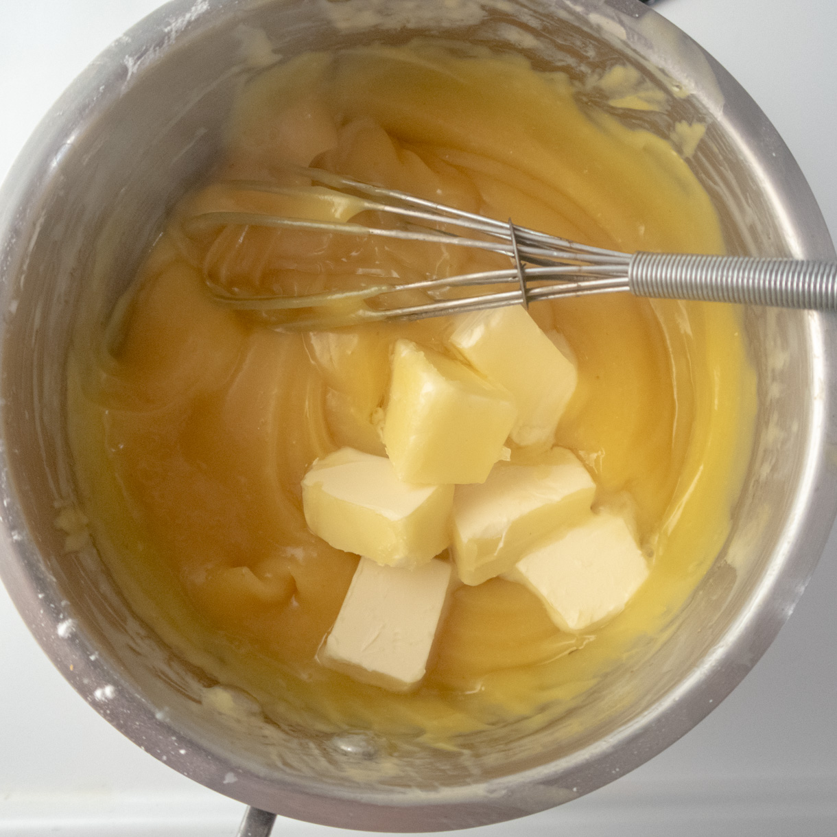 The cooked passionfruit curd in a saucepan with the vegan butter cubes being incorporated.
