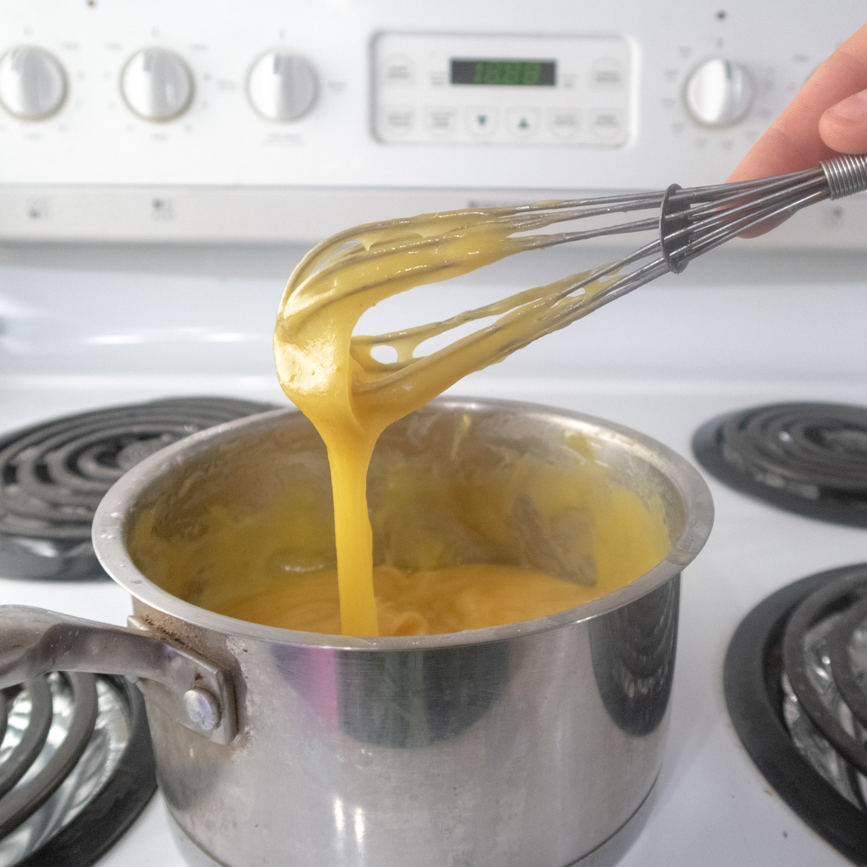 Finished passionfruit curd making a ribbon falling from a wire whisk back into the saucepan.