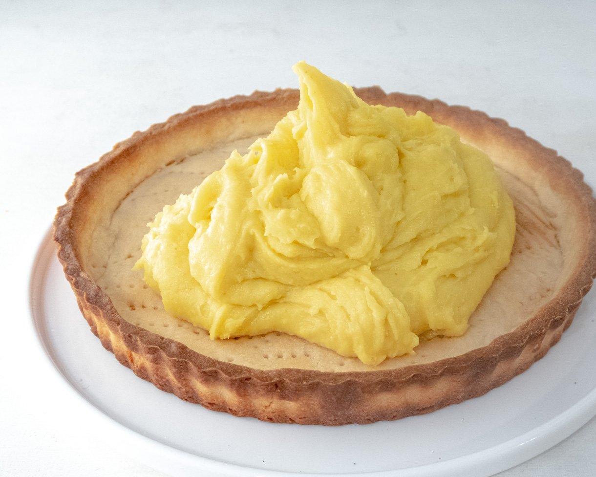 Passionfruit curd being spread in a tart shell.