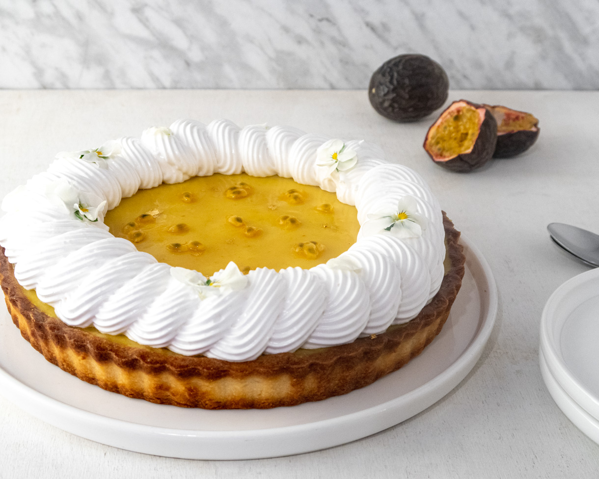Vegan pasisonfruit and meringue tart in front of a white background with half passionfruits in the background.