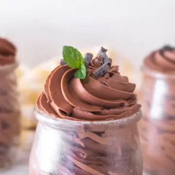 Close up of vegan Baileys chocolate mousse pipped into a glass jar with some mint leaf and chocolate curls on the top.