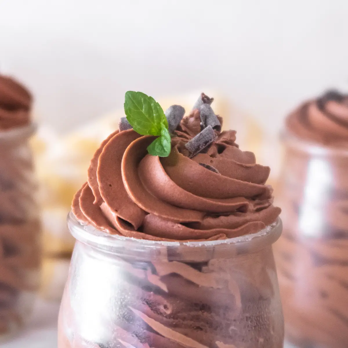 Close up of vegan Baileys chocolate mousse pipped into a glass jar with some mint leaf and chocolate curls on the top.