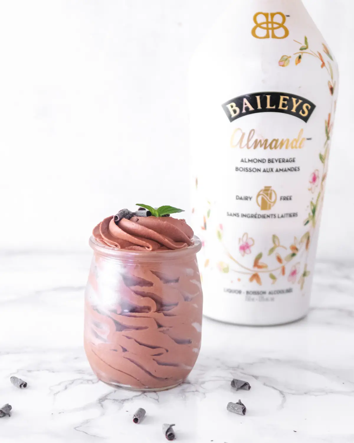 A glass jar filled with vegan Baileys chocolate mousse in front of a bottle of dairy-free Almond Baileys Irish cream.