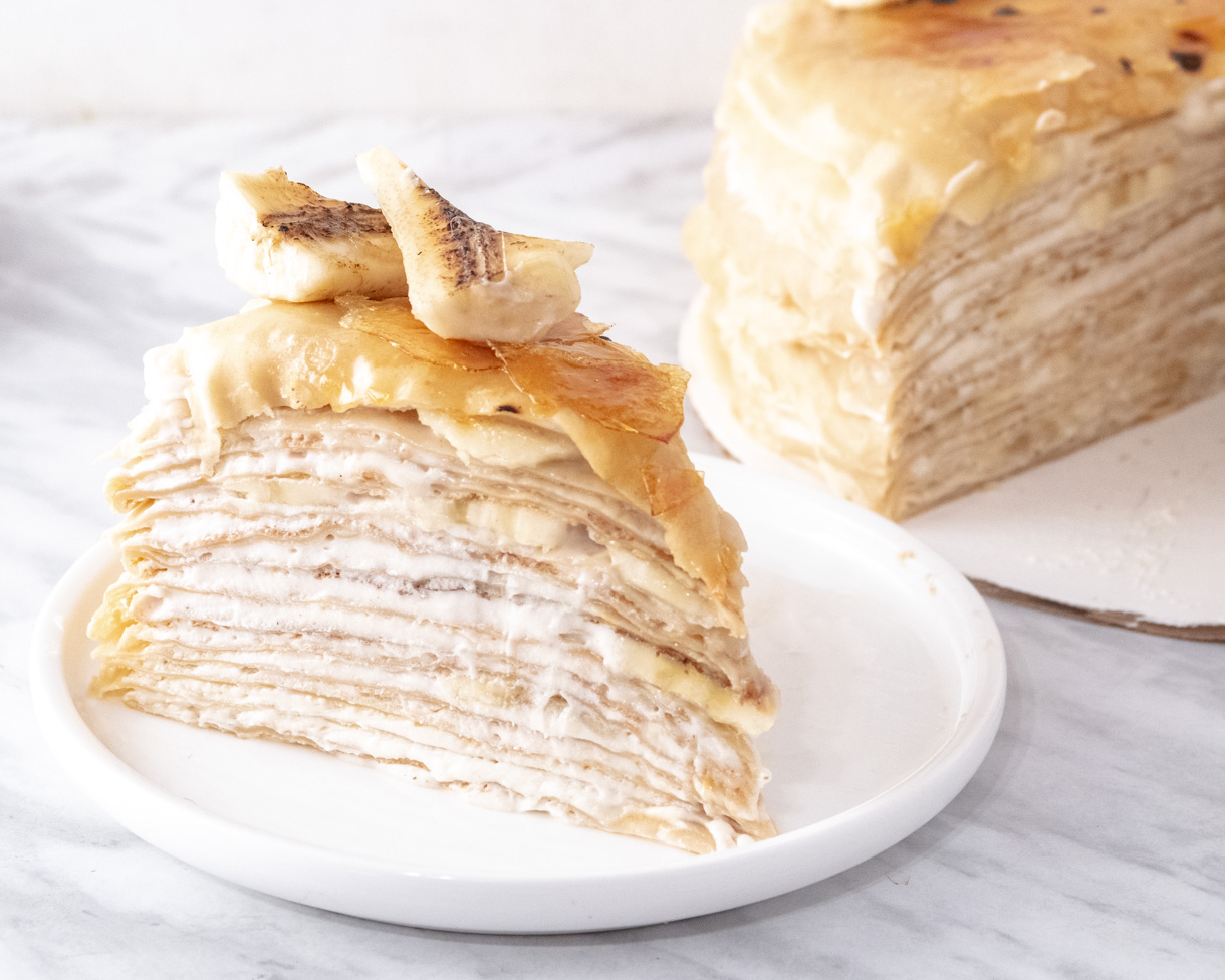 A slice of vegan mille crepe cake on a plate with the rest of the cake in the background.