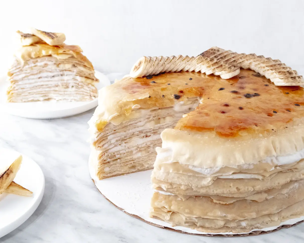Banana bruléed mille crepe cake with a slice taken out to show the layers filled with cream and bananas.