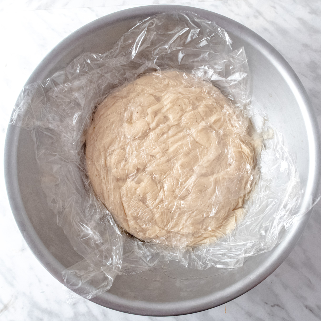 Pastry cream cooling down in a  large mixing bowl with plastic film directly in contact with the surface of the cream.