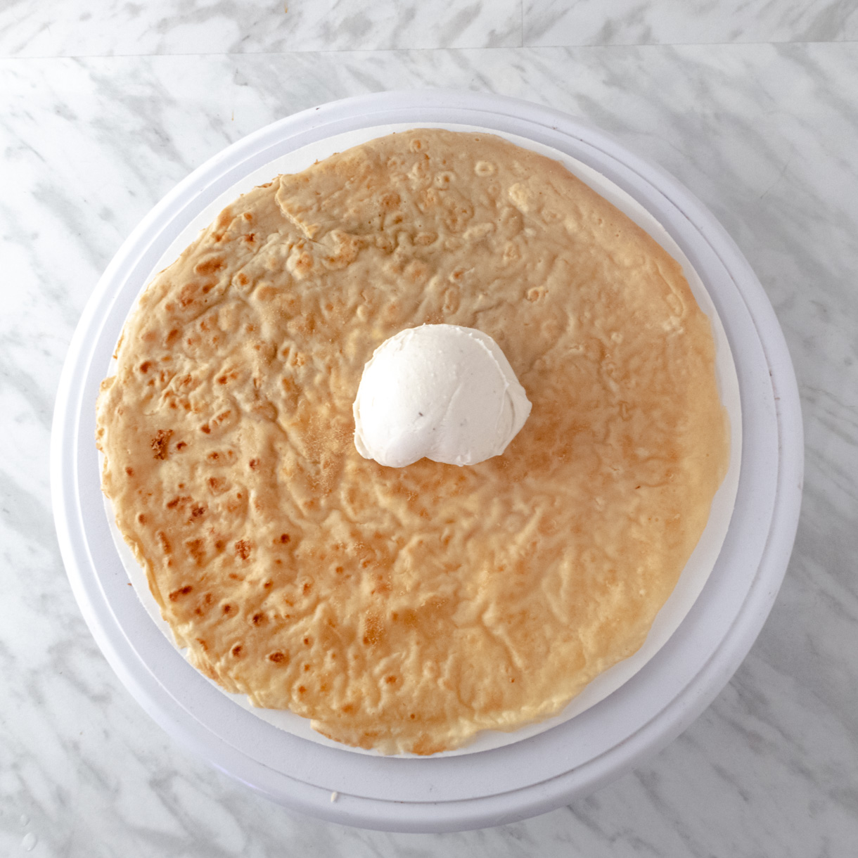 A french crepe on a white cake board with a scoop of crema in the middle to show how much cream to use.