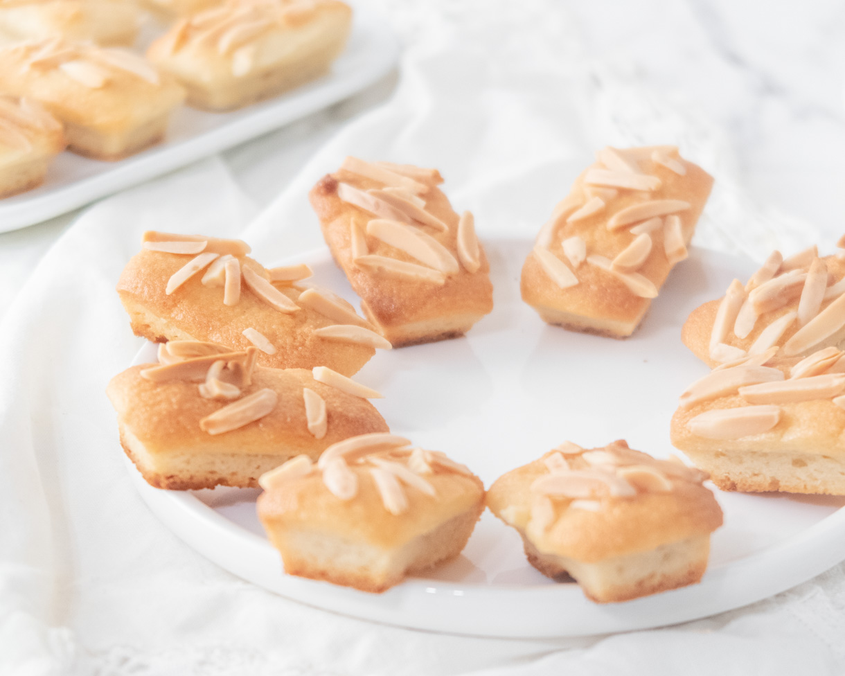 Financiers sprinkled with slivered almond placed in a circle on a round plate.