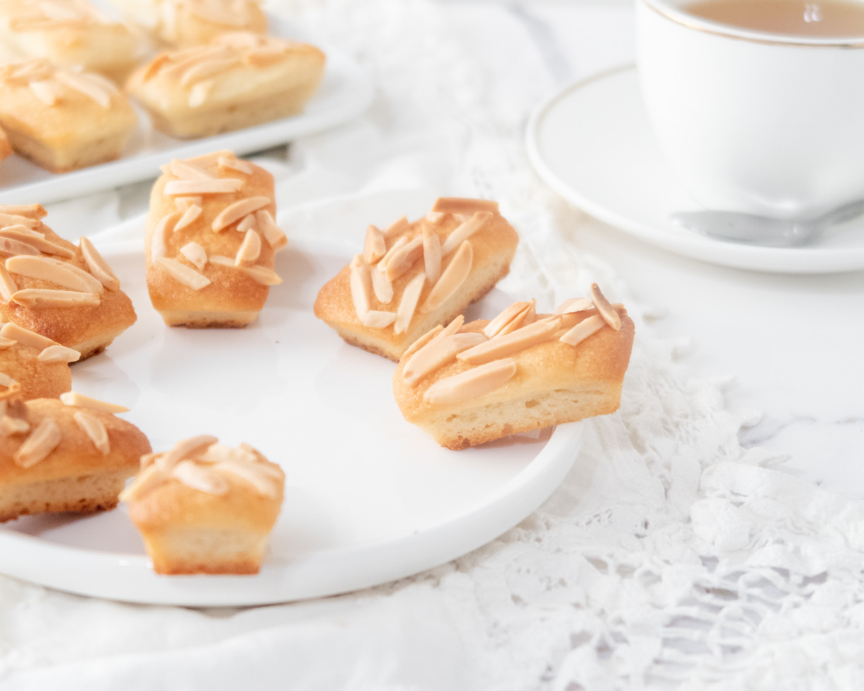 Vegan financiers sprinkled with slivered almond placed in a circle on a round plate.