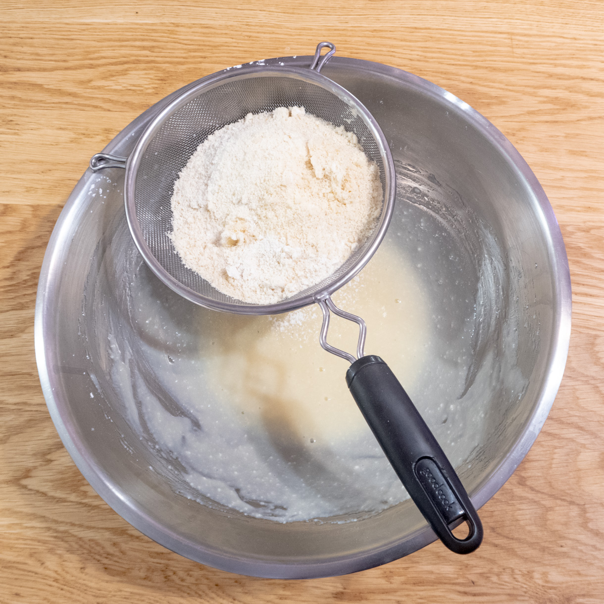 Dry ingredients being sifted on top of the bowl with the whisked tofu and sugar.