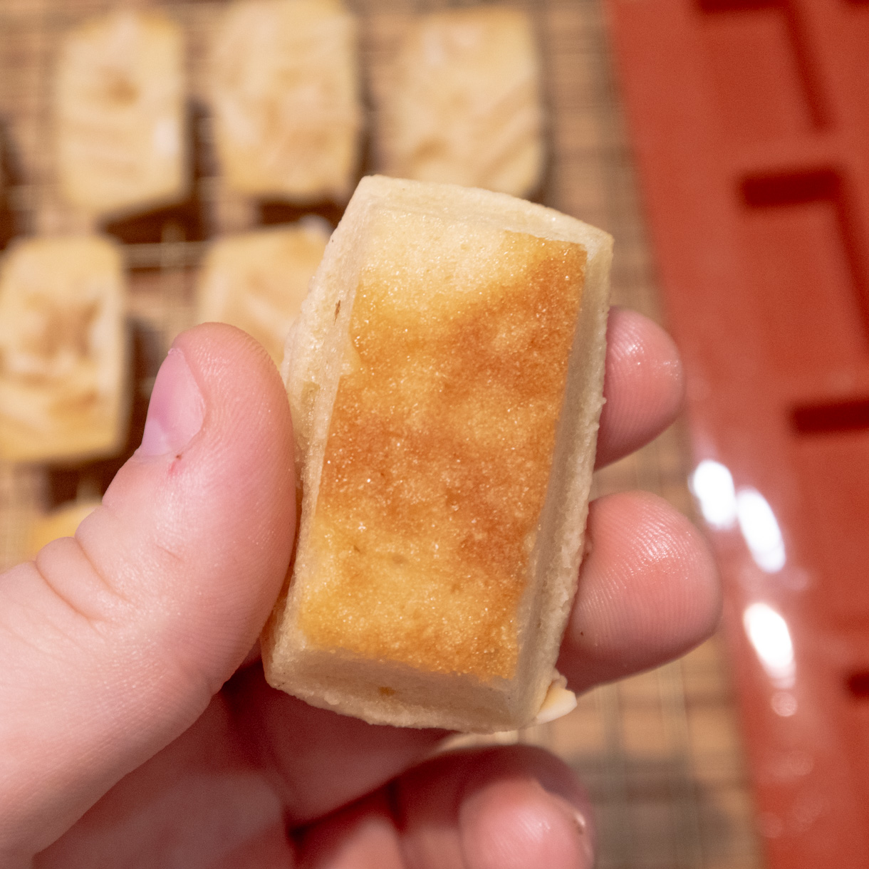 Financier held up upside down to show the golden colour on the underside of the baked good.
