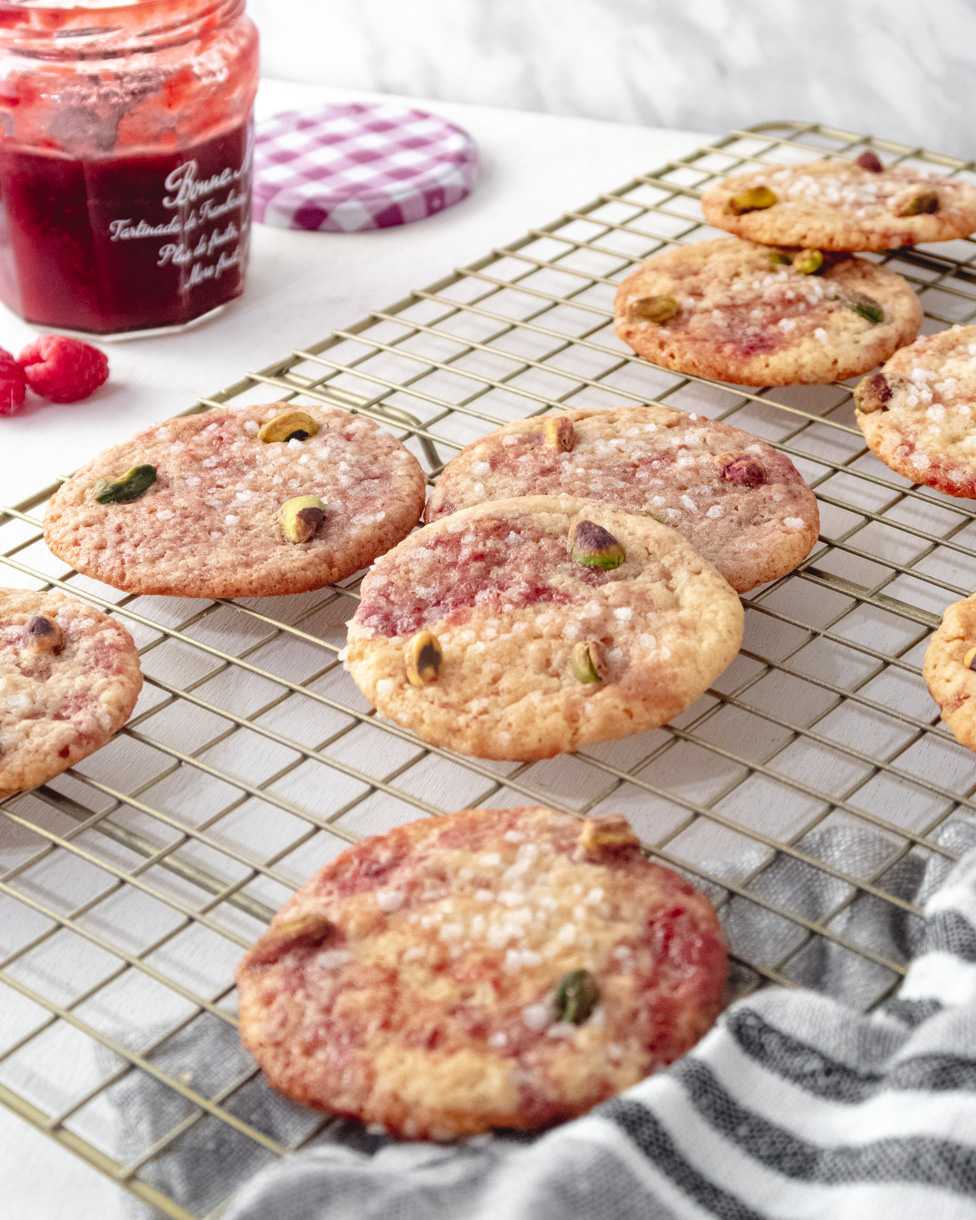 Vegan lemon and raspberry cookies on a golden wire rack with an open jar of raspberry jam in the background