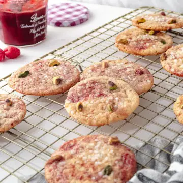 Vegan lemon and raspberry cookies on a golden wire rack with an open jar of raspberry jam in the background