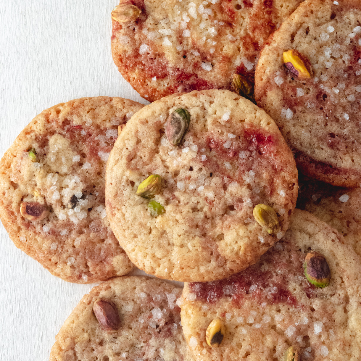 Vegan lemon, raspberry and pistachio cookies piles on top of each other.