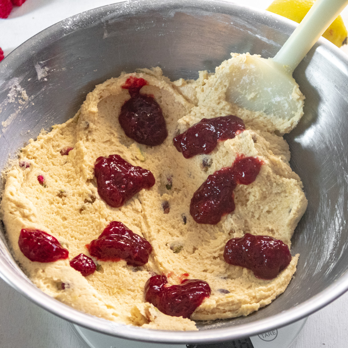 Cookie batter spread in the bottom of a large bowl with 8 dollops of raspberry jam on top of it.