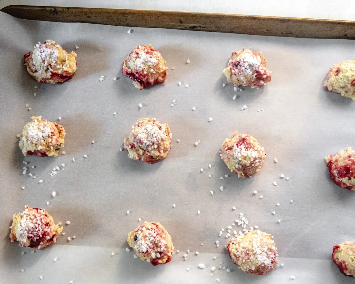 Balls of raw cookie dough covered in pearl sugar on a parchment paper lined baking tray.