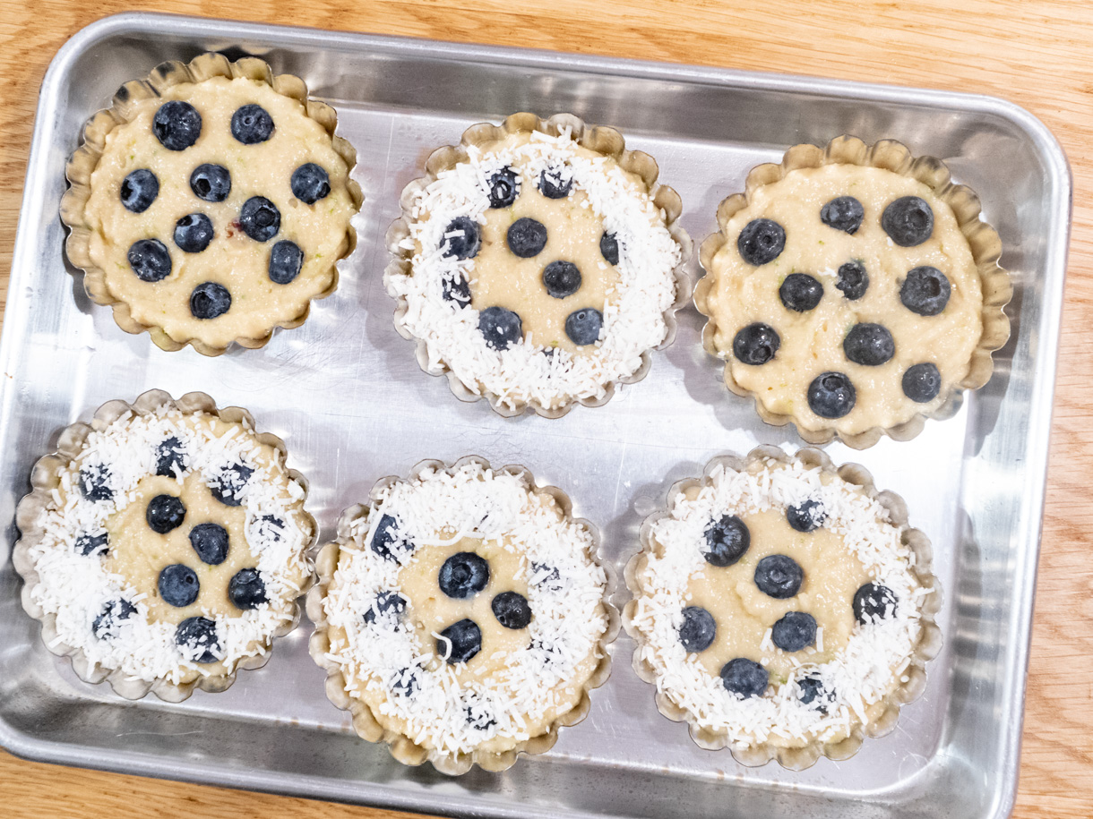 6 blueberry financiers fresh out of the oven still in the tartlet pan on a baking tray.