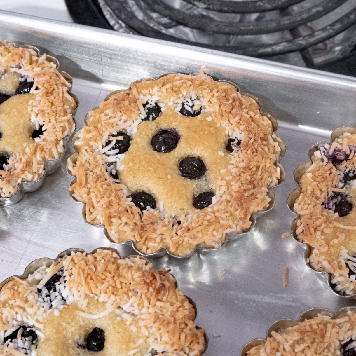 Blueberry financier fresh out of the oven still in the tartlet pan on a baking tray.