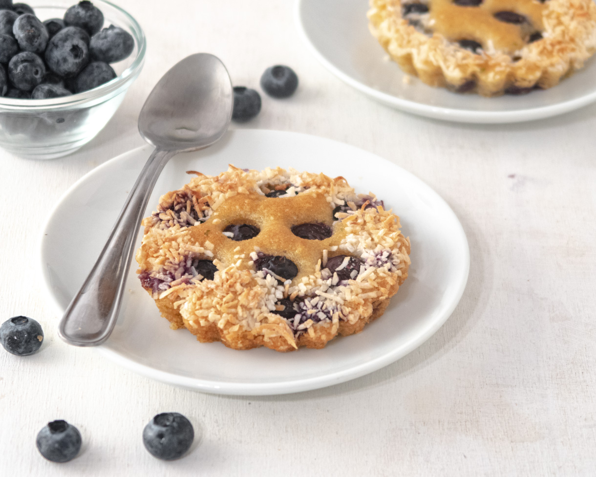 Blueberry and lime financier on a small plate with a spoon and loose blueberries next to it.