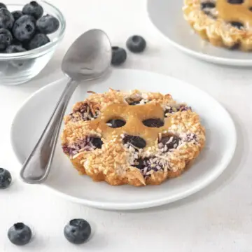 Blueberry and lime financier on a small plate with a spoon and loose blueberries next to it.