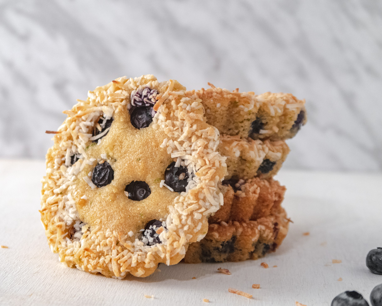 A lime and blueberry vegan financier leaning on 4 stacked financiers in front of a marbled white background.