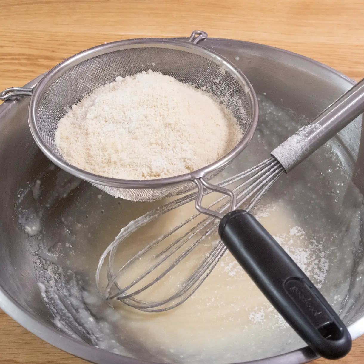 Dry ingredietns being sifted over a bowl with the whisked tofu and sugar mixture.