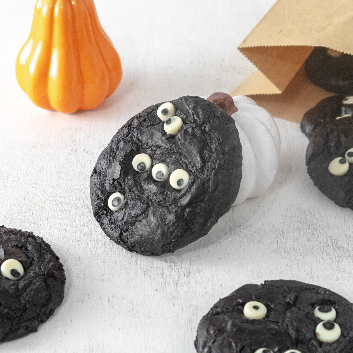Vegan Brownie cookie decorated with monster eyes leaning agains a small white pumpkin with more cookies around it.
