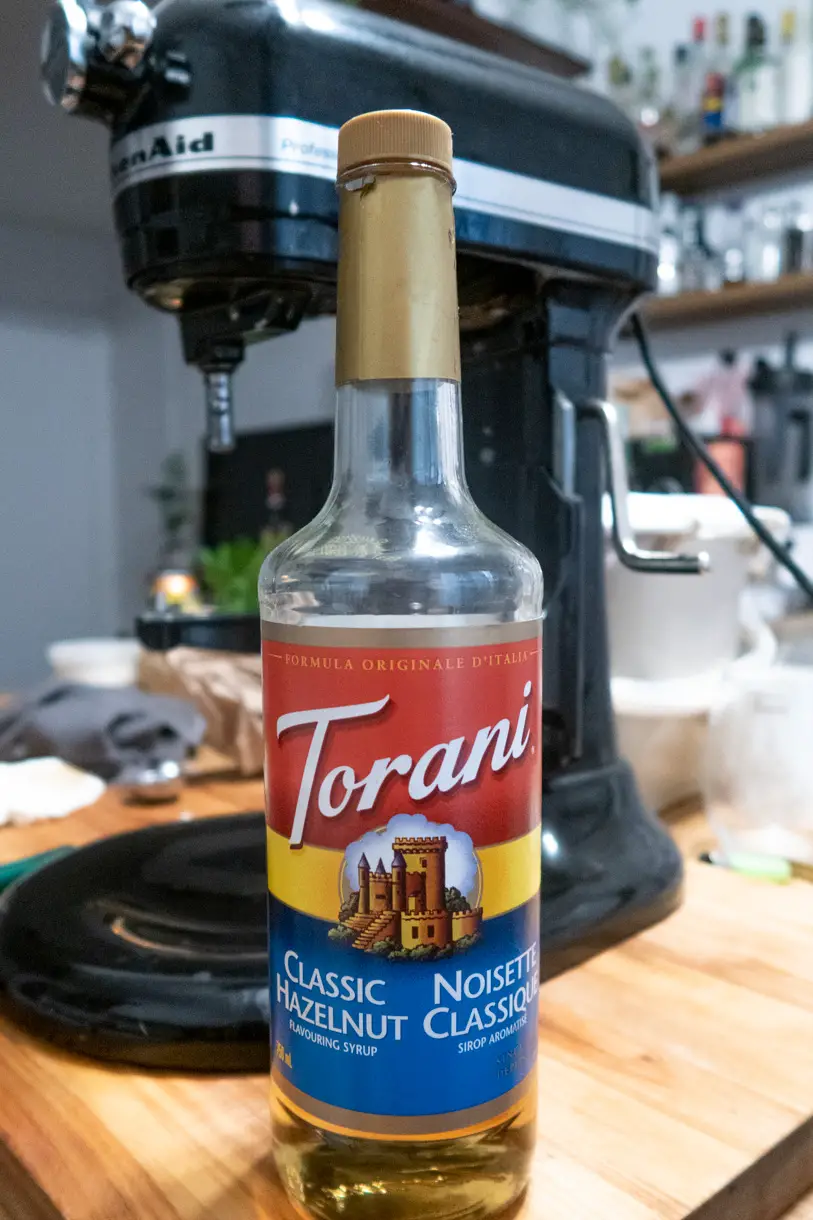 A bottle of Torani Classic Hazelnut syrup in front of a stand mixer.