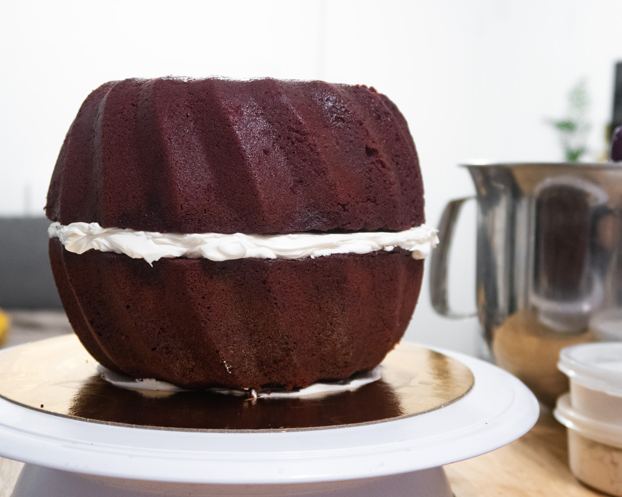 Two vegan red velvet bundt cakes stacked on top of each other with buttercream in the middle to make a sphere.