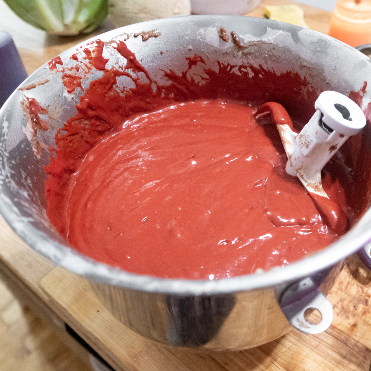 Vegan red velvet cake batter in a large kitchen-aid bowl with the paddle attachment sticking out of the batter.