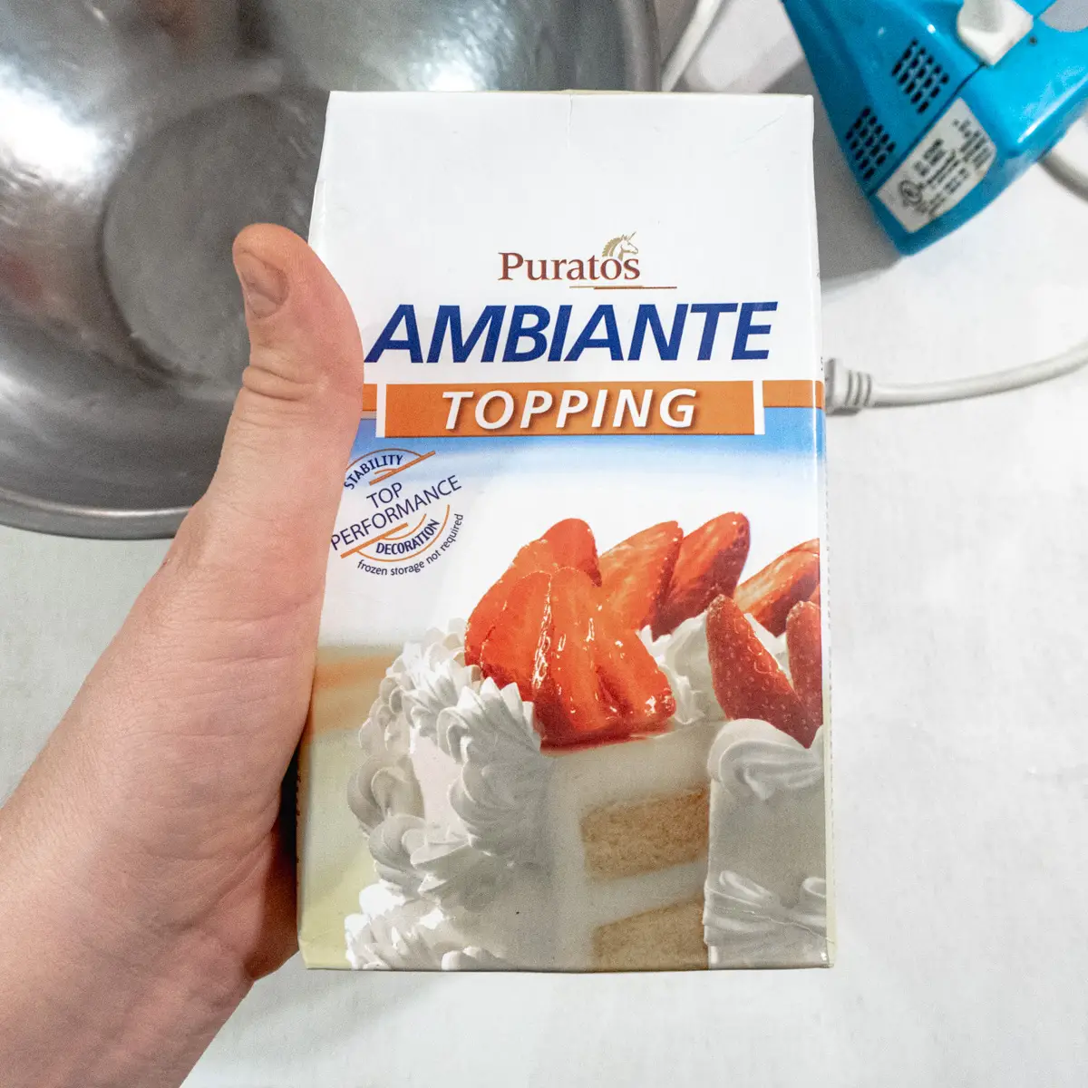 Ambiante vegan whipped cream by the brand Puratos being held up in front of a bowl.