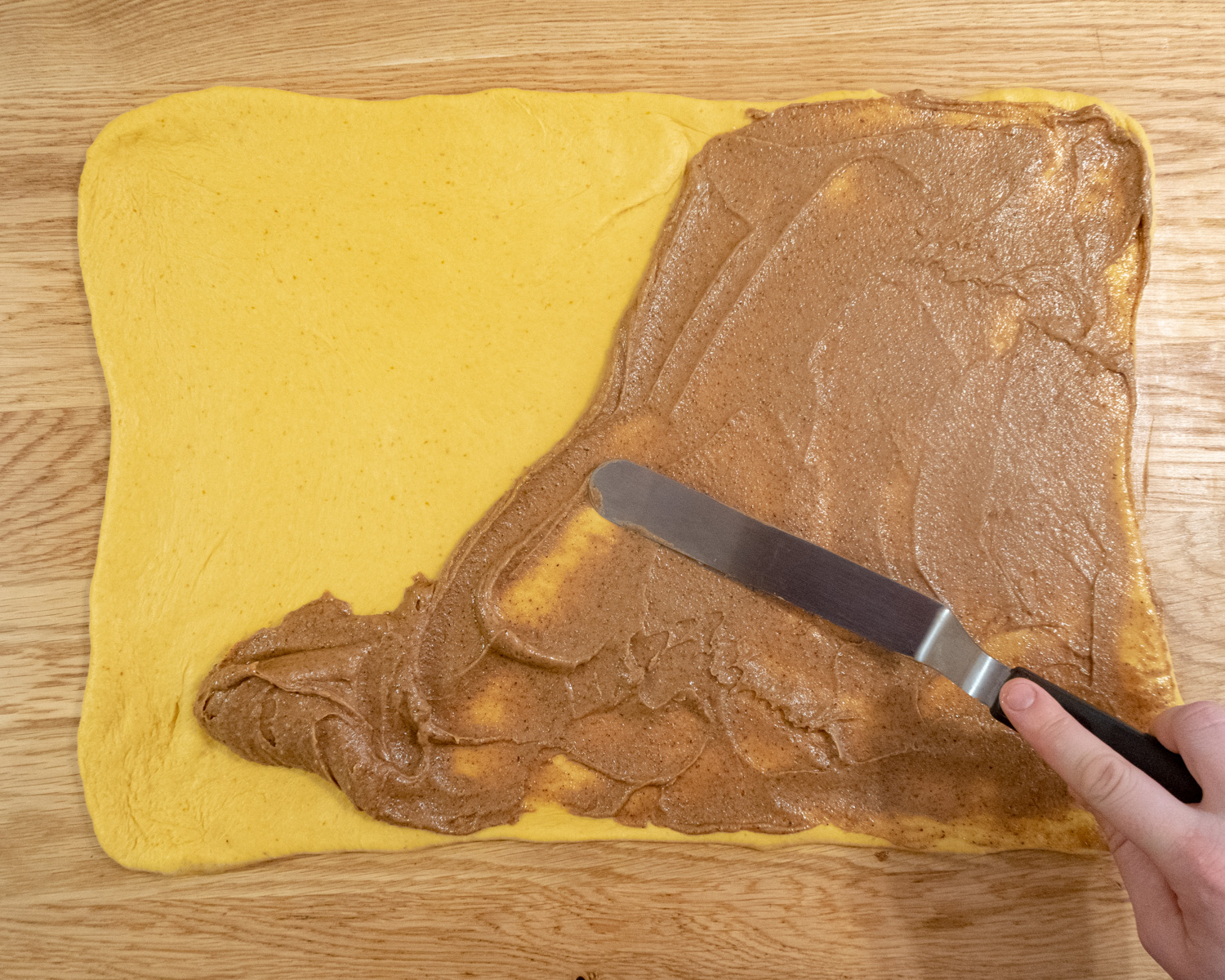 Pumpkin dough rolled out into a rectangle with Biscoff cinnamon filling being spread out on the surface.