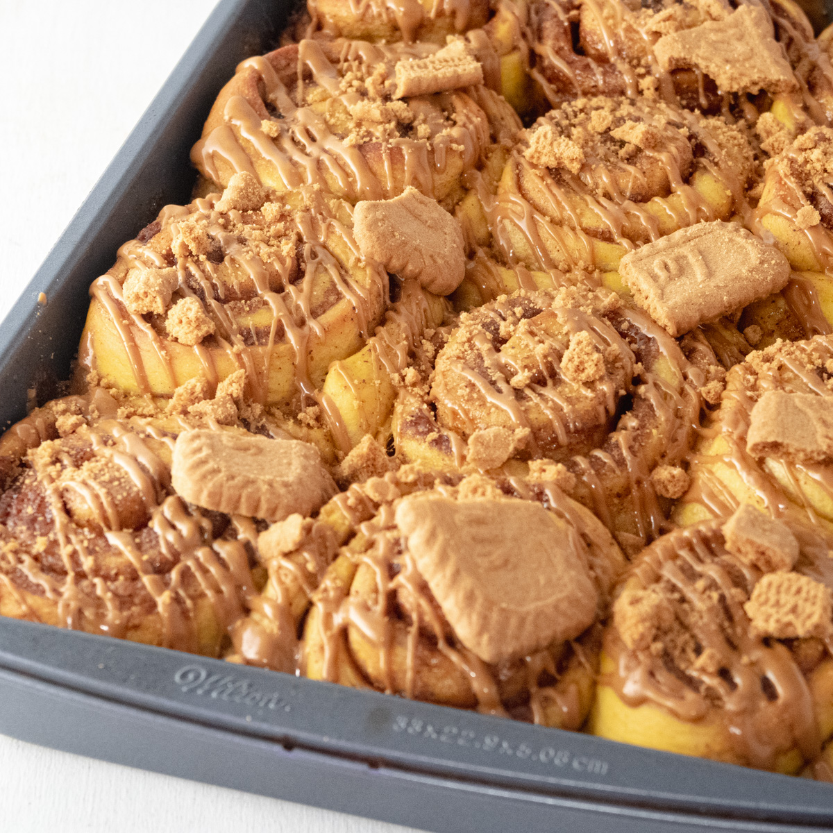 vegan pumpkin cinnamon rolls topped with a drizzle of cookie butter and  crushed Biscoff cookies.