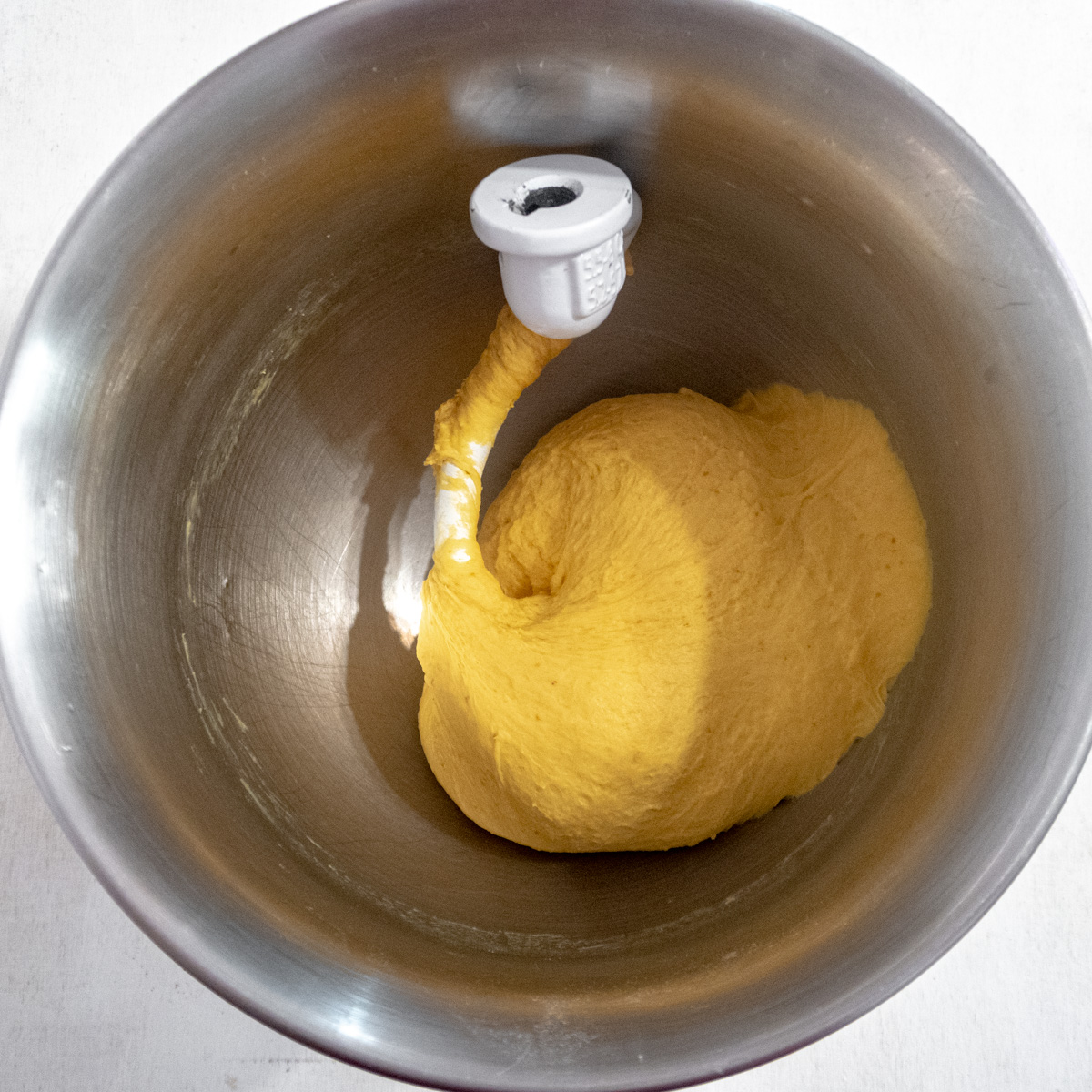 Pumpkin dough kneaded with a dough hook in the bowl of a stand mixer.