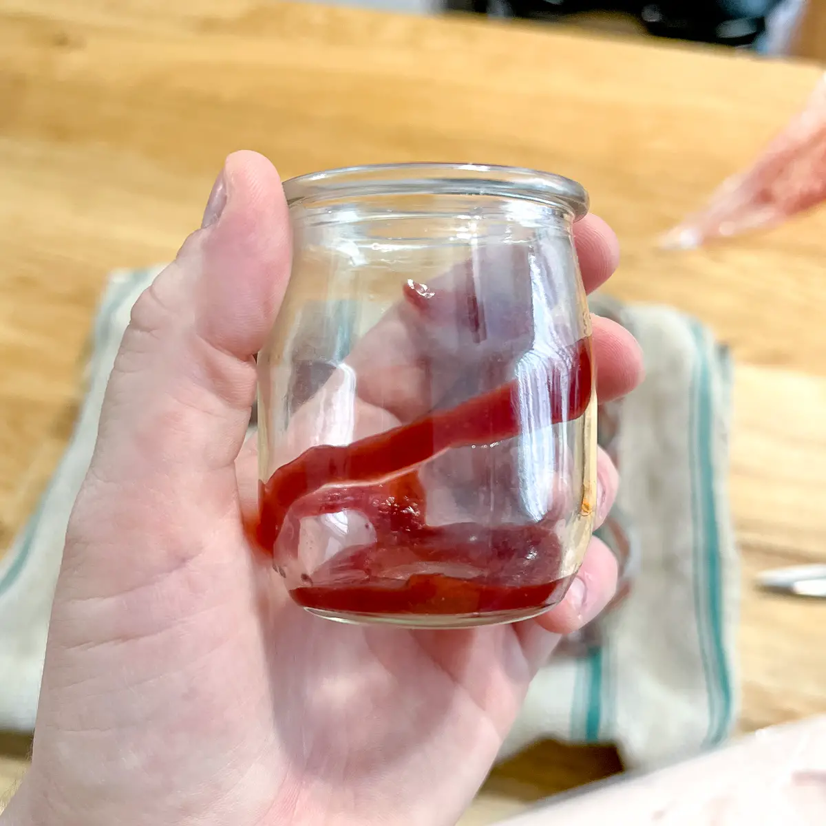 A small glass jar with strawberry sauce drizzle in it.