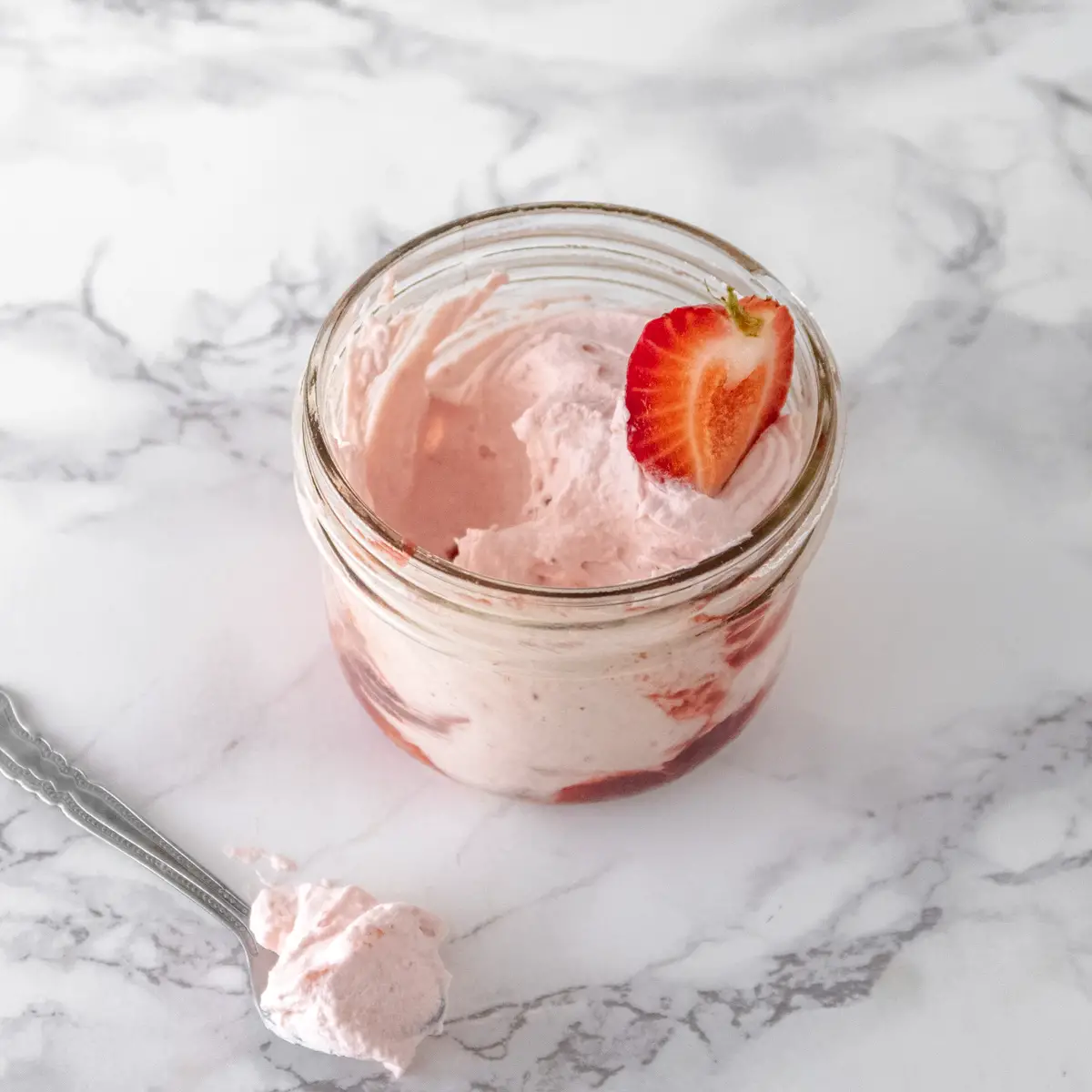 A large jar of vegan white chocolate and strawberry mousse with a bite missing to show the texture of the mousse.